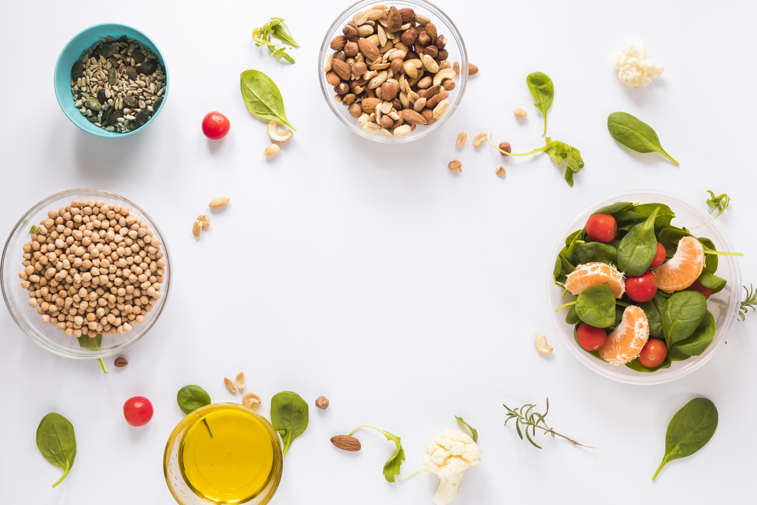 A flat lay of healthy, fresh ingredients including chickpeas, almonds, sunflower seeds, spinach, cherry tomatoes, tangerines, and olive oil, arranged on a white background with copy space in the center. Represents balanced and mindful eating through meal planning